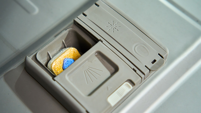 Close-up of a dishwasher's detergent dispenser with a detergent pod inside