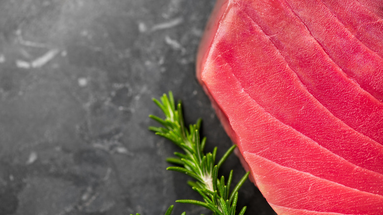 A closeup of a raw tuna steak next to fresh rosemary