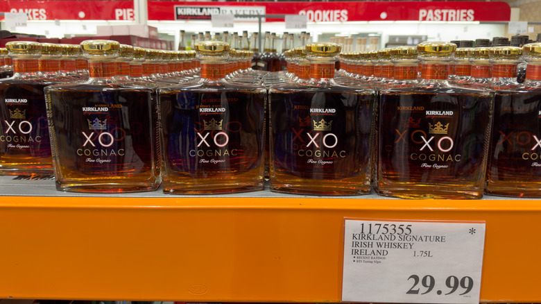 Bottles of Kirkland whiskey on a Costco shelf with a $29.99 price tag with an asterisk