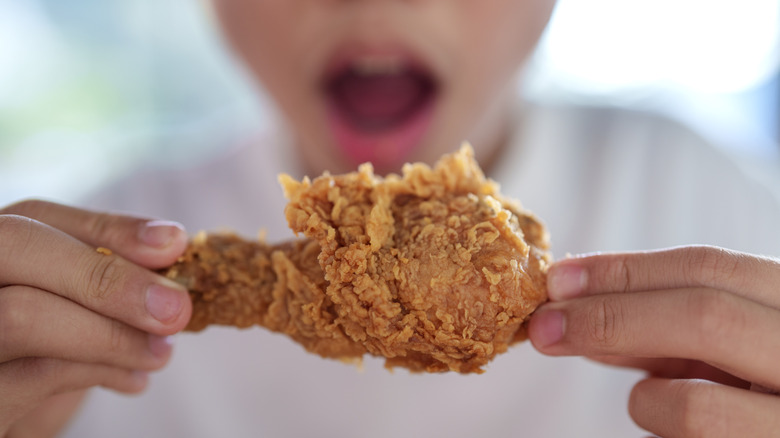 Someone holding a piece of fried chicken in front of them about to eat.