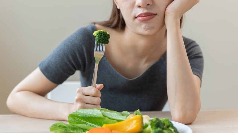 Woman holding fork with broccoli floret on it with undesirable look on her face