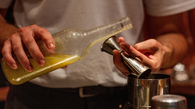 A closeup of a man pouring a citrus juice into a shaker behind a bar