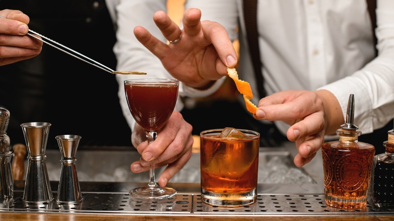 A bartender preparing a cocktail with an orange twist.
