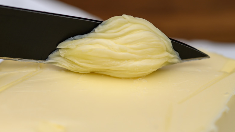 Closeup of a knife scraping butter off a stick of it
