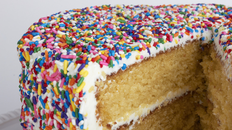 yellow cake with vanilla frosting and sprinkles with slice missing