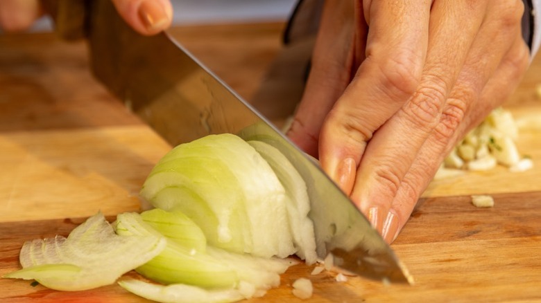 Hand cutting onion on wooden cutting board.