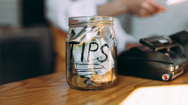 A full tip jar on the counter of a restaurant
