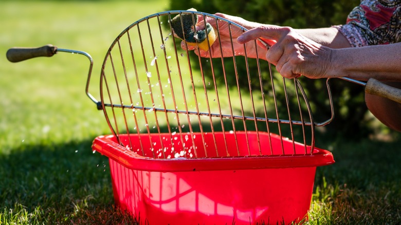 Person cleaning grill grates in bucket with sponge