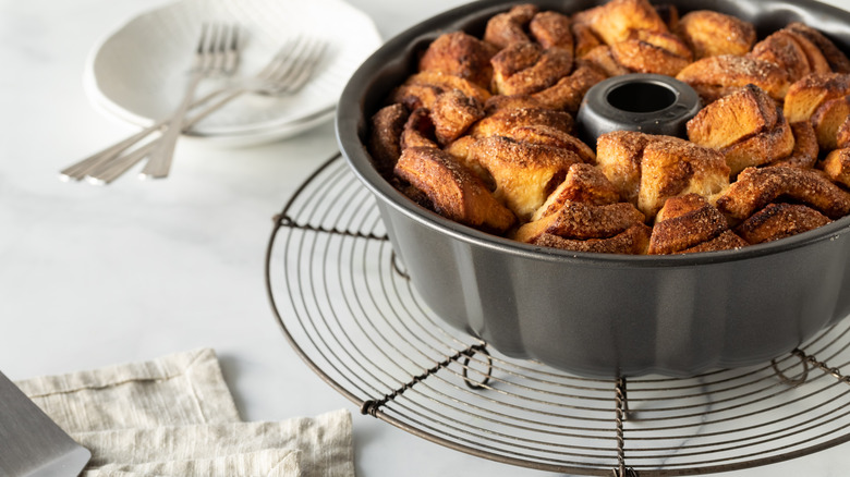 Baked monkey bread in a bundt pan on a white table, with utensils in the background.