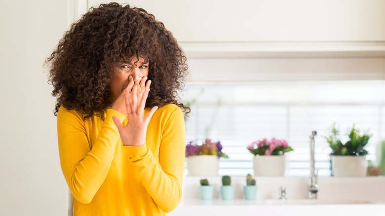 Woman in yellow shirt holding her nose in a kitchen setting