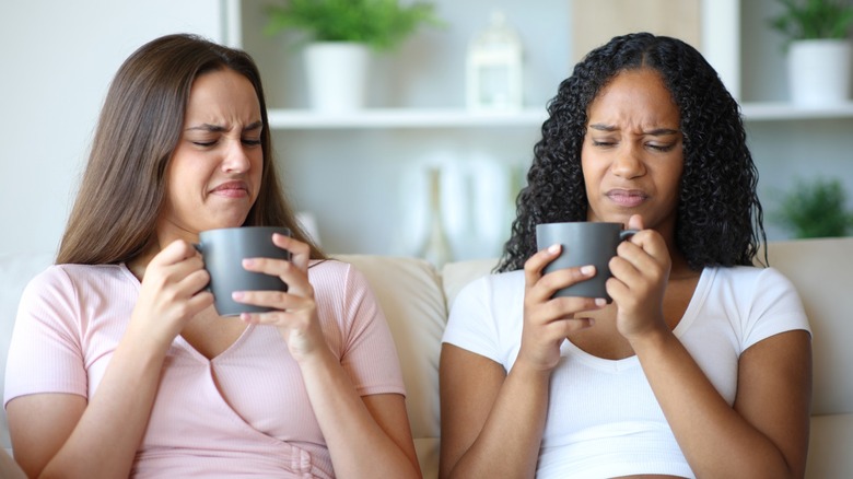 Two people on couch with disgusted facial expressions holding coffee cups