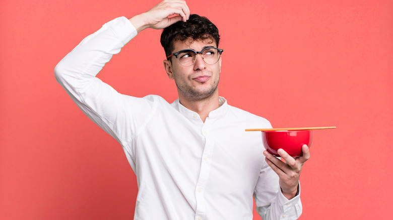 Man scratching his head while holding a bowl with chopsticks