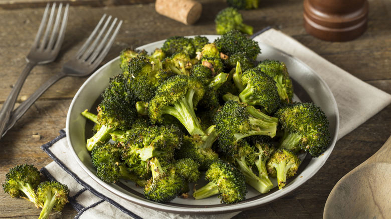 Roasted broccoli in bowl on a wooden surface next to two forks