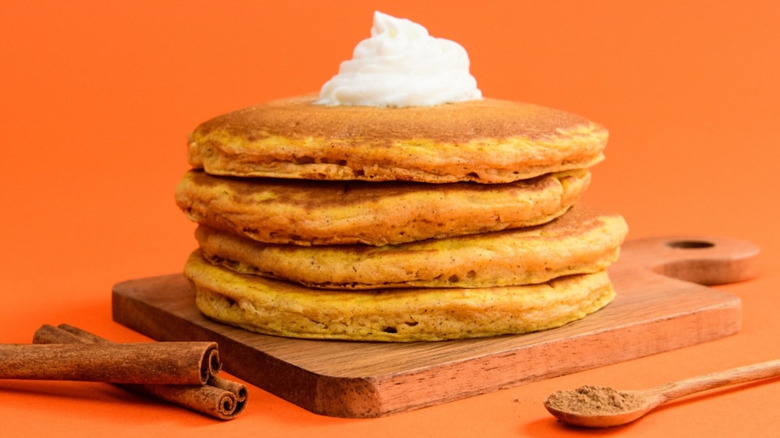 Stack of four pumpkin spice waffles with whipped cream on wooden cutting board from IHOP