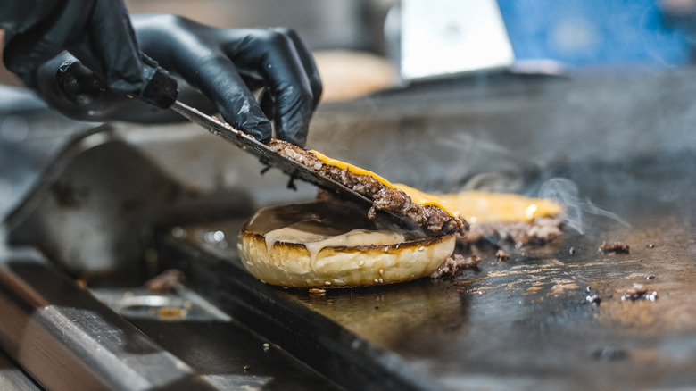Line cook preparing smash burgers on flat top