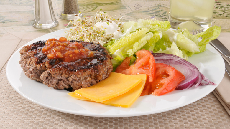 Burger with onions, cheese, tomatoes, and sauce on the side