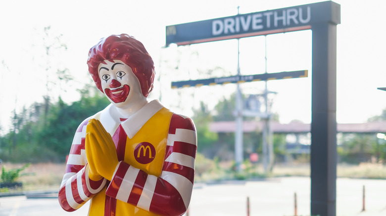 Ronald McDonald at a McDonald's drive-thru with a big smile and his hand held together.
