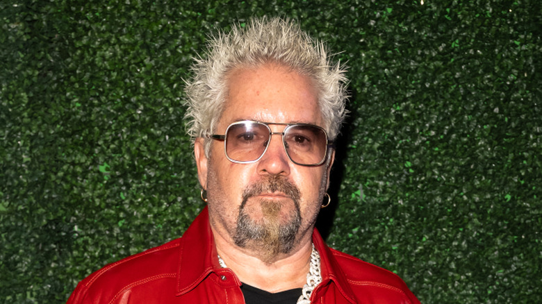 Guy Fieri standing with arms spread behind a kitchen counter
