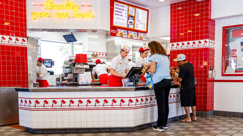 Two customers ordering at the In-N-Out counter with staff in the kitchen in the background