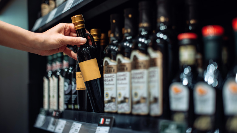 A person selects a bottle of vinegar from a stocked grocery store shelf