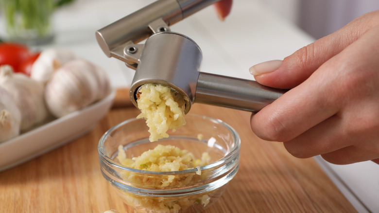 Hands using a garlic press to chop garlic into bowl