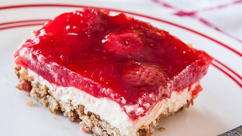 A slice of strawberry Jell-O salad with a pretzel crust on a white plate
