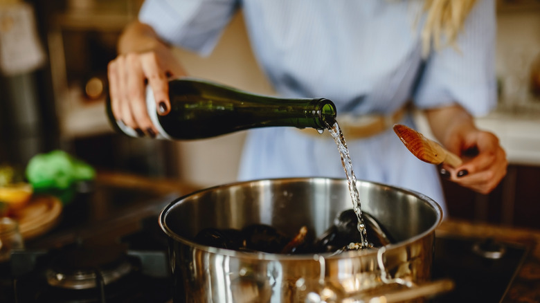 Person adding wine to pot while cooking
