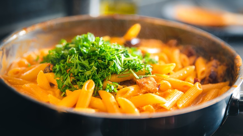 penne a la vodka in a frying pan topped with fresh parsley