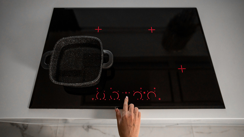 hand turning on an induction stovetop set into a white countertop