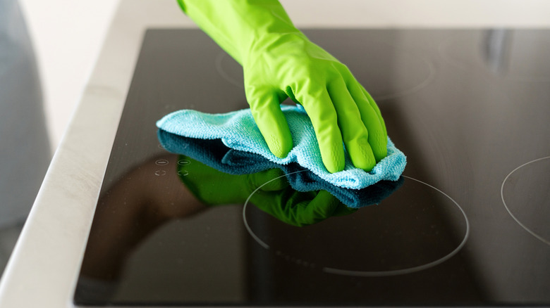 rubber gloved hand using a blue cloth to clean an induction stovetop
