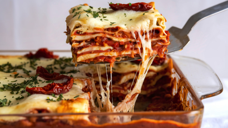 serving utensil removing a piece of lasagna from a clear baking pan