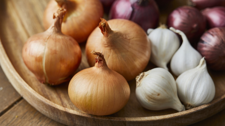 Close up of a variety of onions in a wooden bowl, on a wooden table.