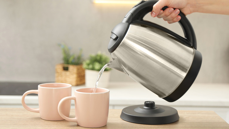 hand pouring water from an electric kettle into a mug
