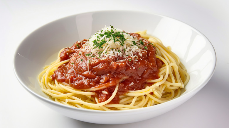 A white bowl of spaghetti noodles with sauce, cheese, and herbs directly on top of it