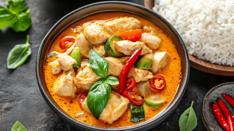 A black bowl of chicken curry with coconut milk, served with a separate bowl of rice