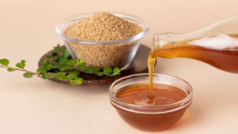 A bowl of sesame seeds and a bottle pouring sesame oil