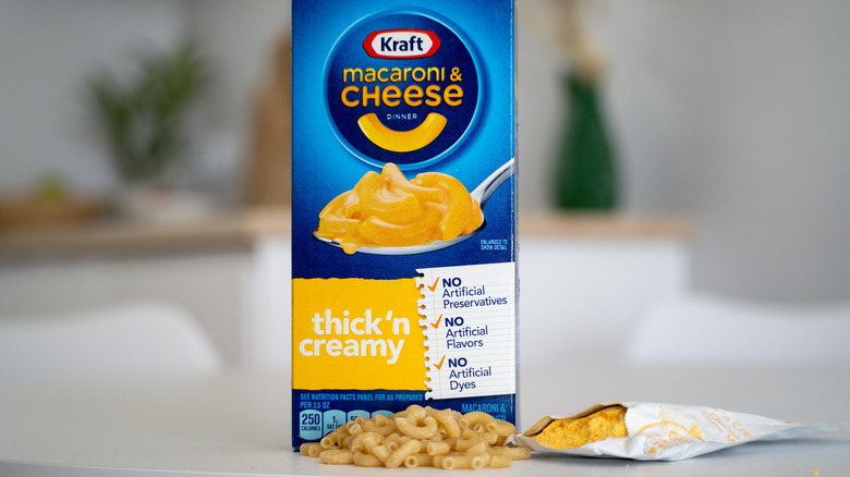 A box of Kraft macaroni and cheese on a white counter with dry noodles and cheese powder beside it