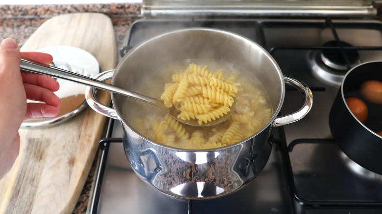 Scooping pasta from a cooking pot with a strainer