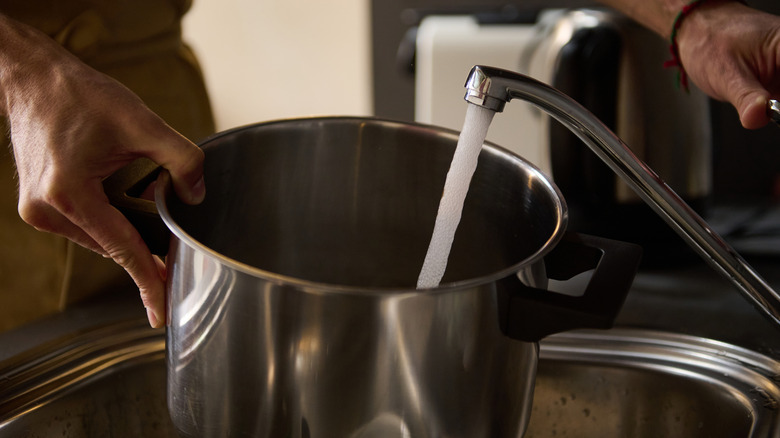 A man fills a pot with water using a sink faucet