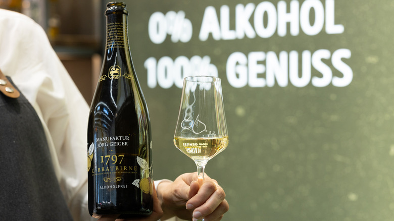 Person holding non-alcoholic sparkling wine bottle and glass