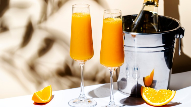Two mimosas next to champagne in bucket and orange slices