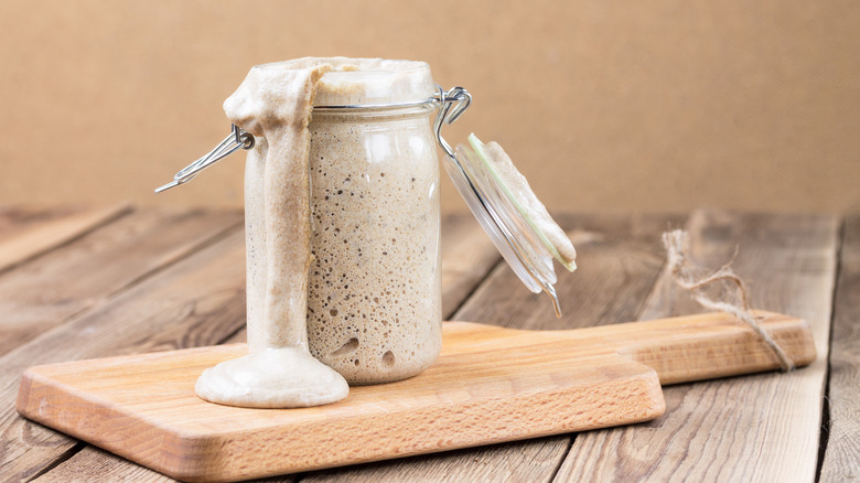 A mason jar of sourdough starter overflowing onto a cutting board.