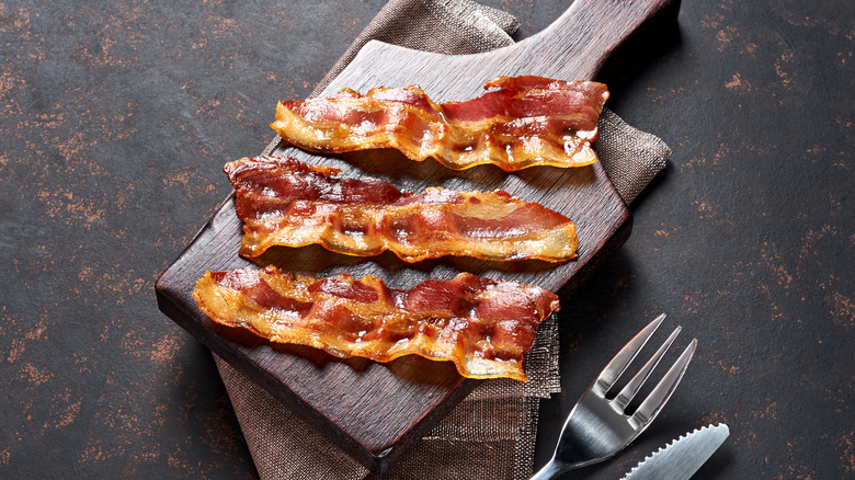 Three slices of cooked bacon on wood board with linen