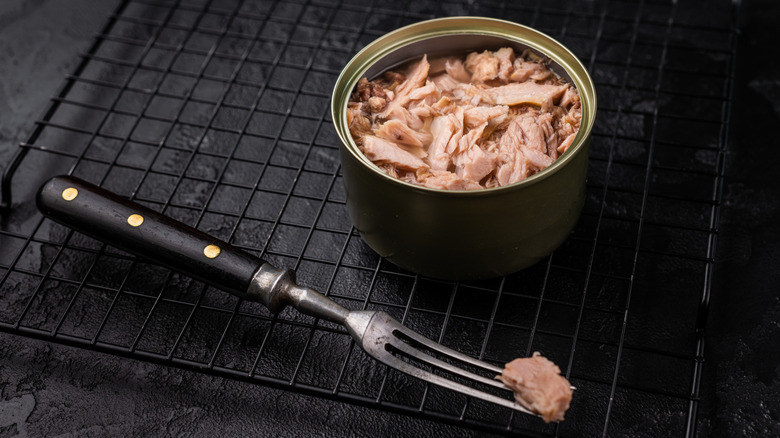 an open can of tuna and a fork sitting on a dark background
