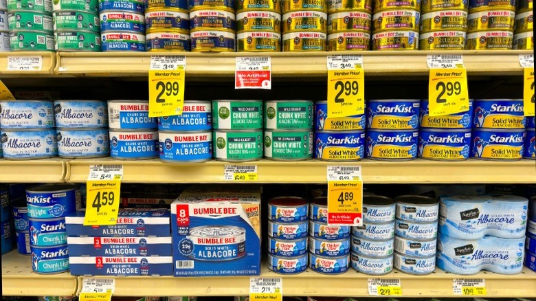 Various brands of canned tuna sitting on grocery shelves