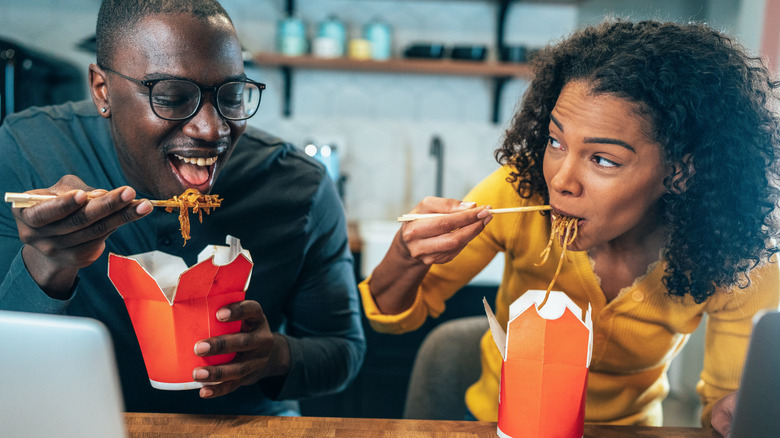 A couple enjoying two boxes of Chinese takeout noodles