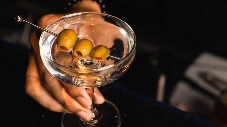 Person holding martini with olive garnish