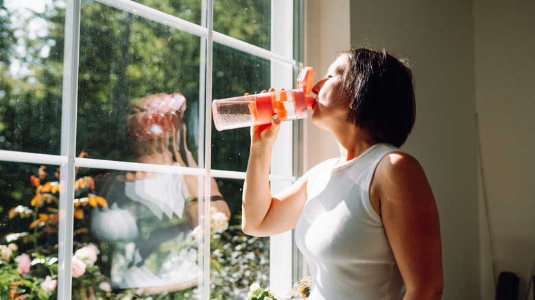 Person drinking water in their kitchen in front of the window