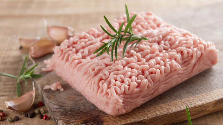 Raw pink ground turkey or chicken topped with a rosemary sprig on a wooden cutting board