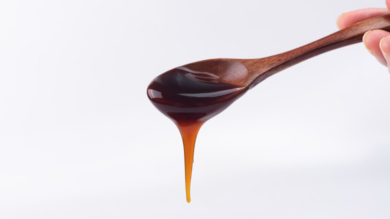 A hand holds a wooden spoon from which oyster sauce drips